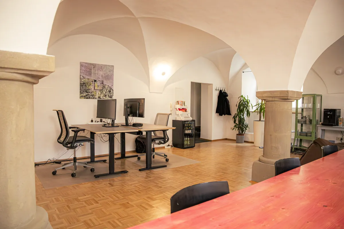 Coworking Space in Dinkelsbühl: Gewölbe mit Säulen, höhenverstellbare Schreibtische und ein langer pinker Tisch